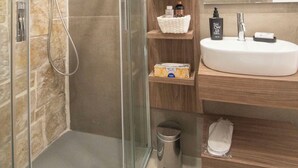 A modern bathroom with a glass-enclosed shower, a wooden vanity with a sink, and a mirror above the vanity. - my Vesta Suites (Vieste)