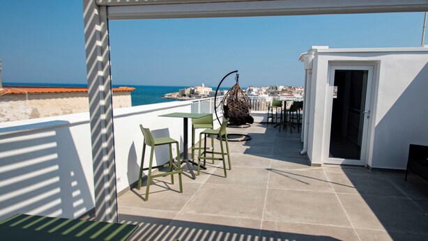 A terrace with a view of the sea, featuring a table and chairs, a hanging chair, and a door leading to a room. - my Vesta Suites (Vieste)