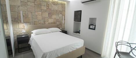 Une chambre avec un mur en pierre, un lit, une table de chevet, une chaise et une fenêtre avec des rideaux.