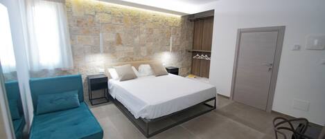 A bedroom with a bed, a blue sofa, a stone wall, a wooden wardrobe, and a door.