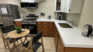 A modern kitchen with a central island, wooden cabinets, stainless steel appliances, and a dining area with a round table and chairs. - The Perfect Getaway (Orangeville)