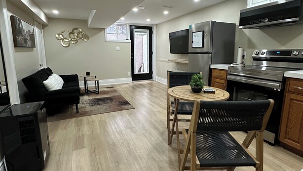 A modern kitchen with a built-in oven, microwave, and stove. There is a dining area with a round table and two chairs. A black sofa and a small side table are in the living area. - The Perfect Getaway (Orangeville)