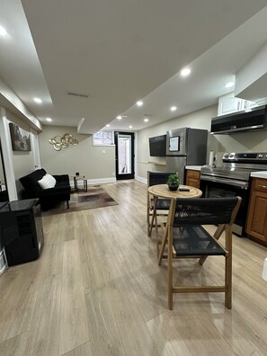 A modern kitchen with a built-in oven, microwave, and stove. There is a dining area with a round table and two chairs. A black sofa and a small side table are in the living area. - The Perfect Getaway (Orangeville)