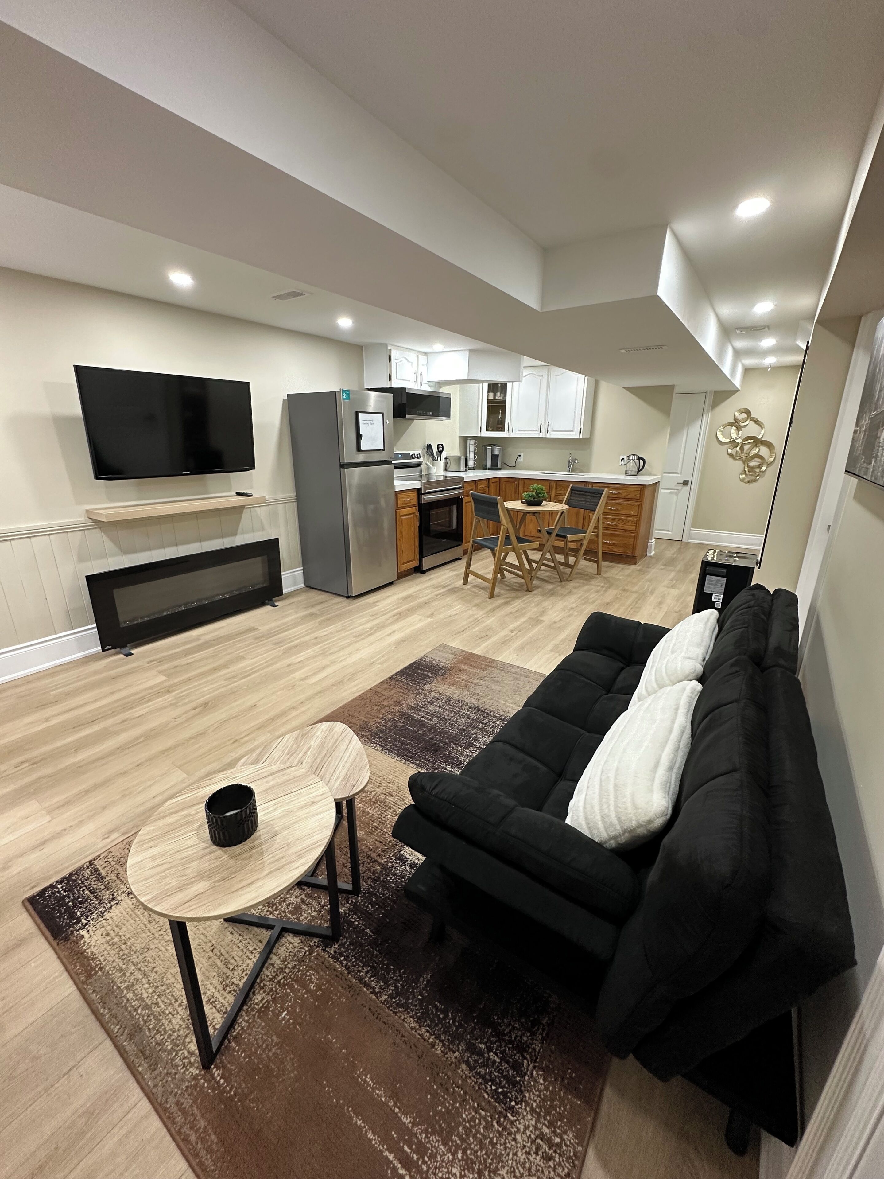 A modern living room with a black sofa, a small round table, and a flat-screen TV mounted on the wall.