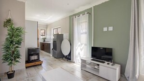 A modern living room with a flat-screen TV, a white entertainment unit, a potted plant, and a large window with curtains.