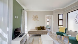 A modern living room with a sofa, a coffee table, and a TV. There are two chairs and a small table with a decorative item.