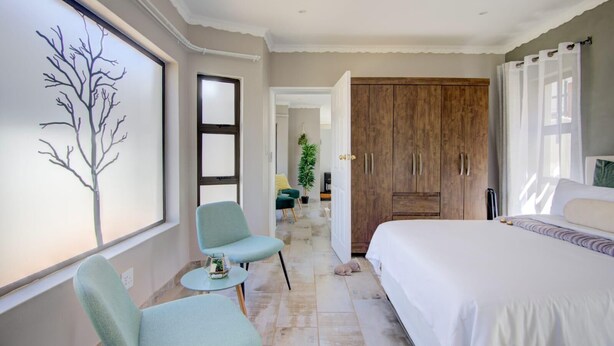 A bedroom with a large bed, a chair, a small table, and a wardrobe.