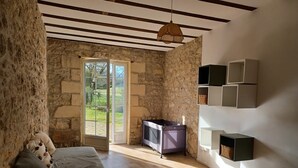 A rustic room with stone walls, a wooden floor, a bed with pillows, a television, and a hanging light fixture. - Large family home with swimming pool for 10 people (Puisseguin)