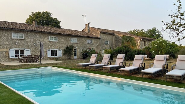 A swimming pool with lounge chairs and a stone building in the background. - Large family home with swimming pool for 10 people (Puisseguin)