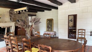 A dining area with a round wooden table surrounded by wooden chairs, a vase with dried plants, a mirror, and a stone wall. - Large family home with swimming pool for 10 people (Puisseguin)