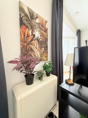 A room with a white radiator, a flat-screen TV on a black stand, and three potted plants on a white console table.