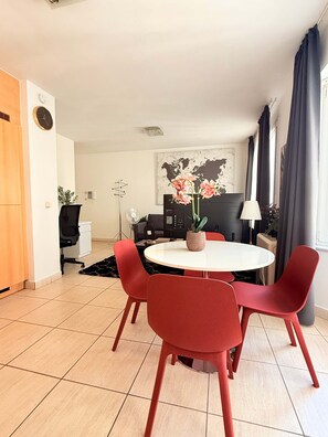 A modern living room with a round dining table, red chairs, a black sofa, a world map artwork, and a large window with curtains. - Bright & Refined Apartment in the Heart of the EU Quarter (Brussels)