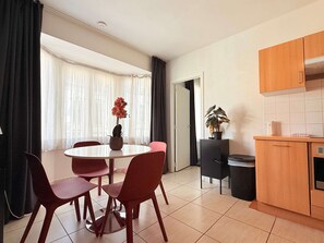 A modern kitchen with a dining area, a potted plant, and a view through the window.