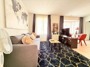 Ein Wohnzimmer mit einer Couch, einem Couchtisch, einem Fernseher und einem Essbereich mit Stühlen.