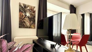 A modern living room with a flat-screen TV, a lamp, and red chairs.