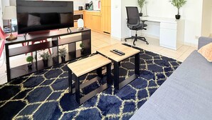 Un soggiorno moderno con una TV a schermo piatto, un divano, un tavolino da caffè e una cucina sullo sfondo.