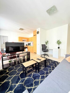 A modern living room with a flat-screen TV, a sofa, a coffee table, and a kitchen in the background. - Bright & Refined Apartment in the Heart of the EU Quarter (Brussels)