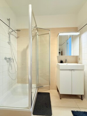 A modern bathroom with a glass shower enclosure, a white sink, and a mirror. - Bright & Refined Apartment in the Heart of the EU Quarter (Brussels)