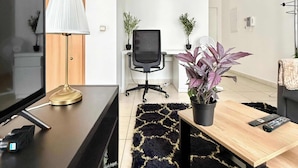 A modern living room with a TV, a lamp, a desk, a chair, and two potted plants.