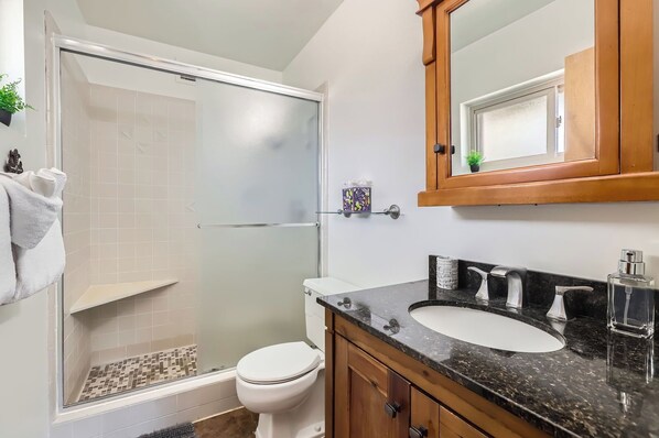 Un baño con cabina de ducha de vidrio, inodoro, lavamanos con encimera de mármol y un armario de madera.