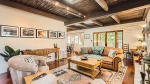 Uma sala de estar aconchegante com teto de madeira, um sofá, uma mesa de centro e um espaço de jantar com mesa e cadeiras.