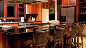A modern kitchen with wooden cabinets, a large island with bar stools, stainless steel appliances, and a high ceiling with exposed beams.