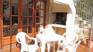 Un patio con sillas de plástico blanco, una mesa, un muro de piedra y una zona de barbacoa.