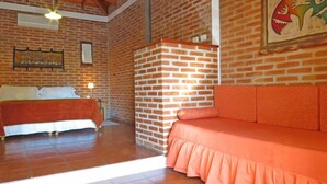 Una habitación con pared de ladrillo, una cama con colcha blanca y naranja, cabecero de madera y un sofá con cojín naranja.