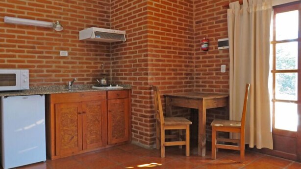 Una cocina con pared de ladrillo, microondas, pileta y mesa de madera con sillas.