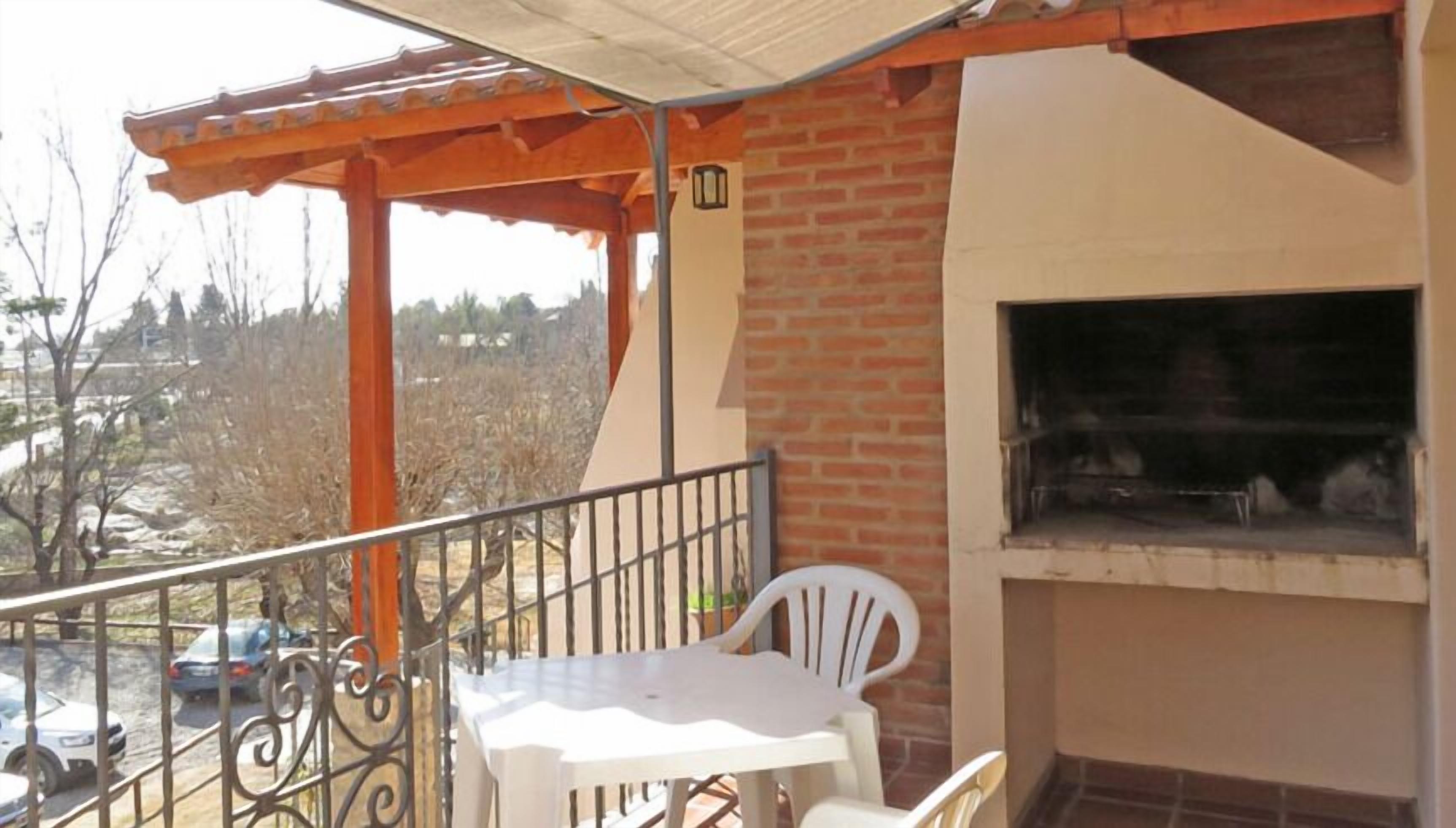 Un balcón con muro de ladrillo, una mesa blanca, una silla blanca y una parrilla.