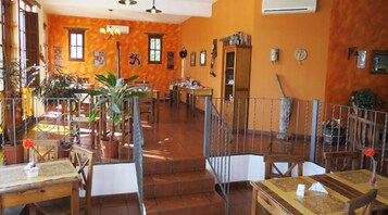 A spacious indoor area with multiple tables and chairs, a staircase, and various potted plants.