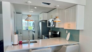 A modern kitchen with white cabinets, stainless steel appliances, and pendant lighting. - Beachfront Top Corner Condo, Sunrise & Sunset Views, Renovated, Sleeps 6 (Fort Myers Beach)