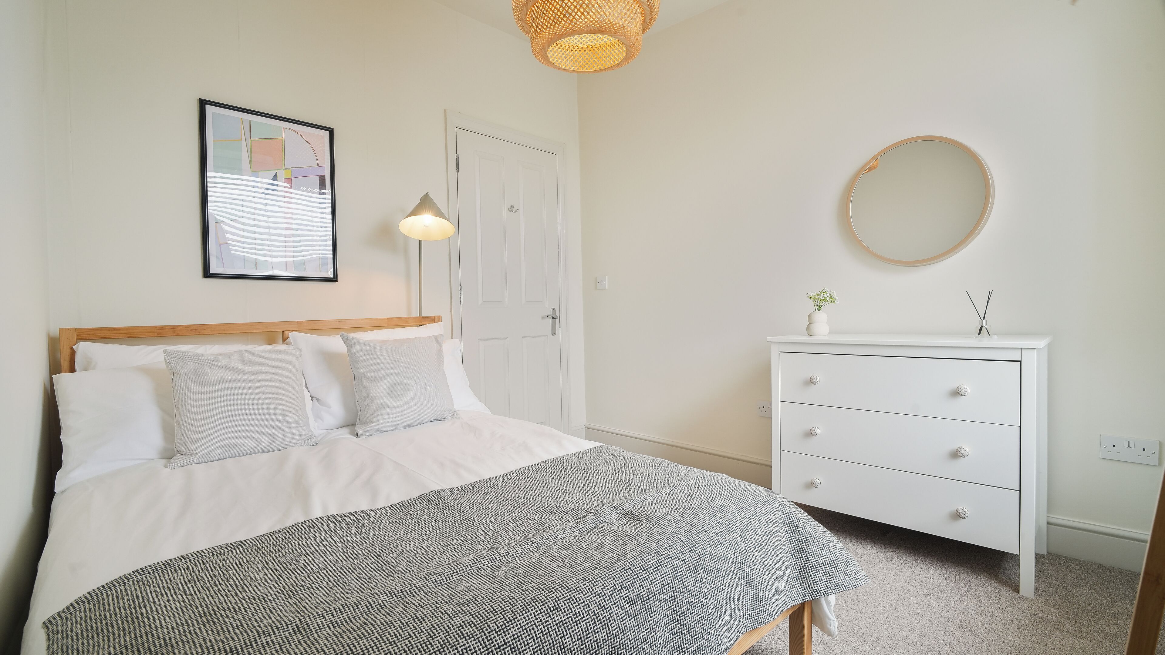 A bedroom with a bed, bedside table, dresser, and a framed picture on the wall.