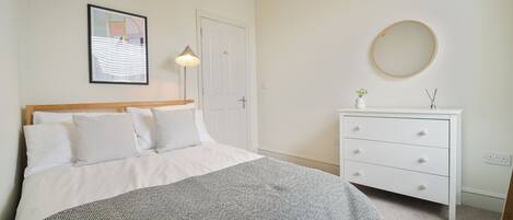 A bedroom with a bed, bedside table, dresser, and a framed picture on the wall.