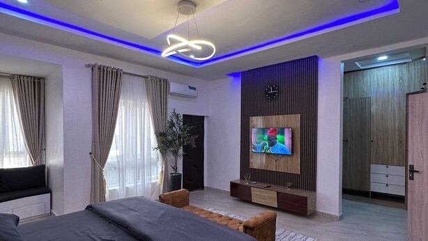 A modern bedroom with a large bed, a TV mounted on the wall, and a ceiling with blue LED lighting.