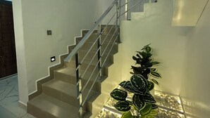 A modern staircase with a metal railing, leading to a landing with a potted plant and a lighted pebble bed.