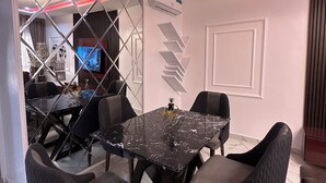 A modern dining area with a glass-top table, dark upholstered chairs, and a geometric wall design.