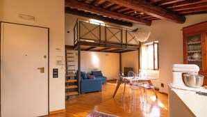 A spacious living area with a loft bedroom, wooden beams, a dining table with chairs, and a kitchen area with a mixer. - Elegant apartment with panoramic terrace in the historic heart of Pistoia (Pistoia)