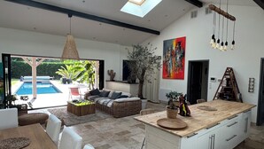 A spacious living area with a large island, a dining table, and a view of a swimming pool. - Indonesian villa (Lacanau)