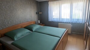 Una habitación con una cama de madera, una mesita de noche, una lámpara y un ventanal con cortinas de gasa.