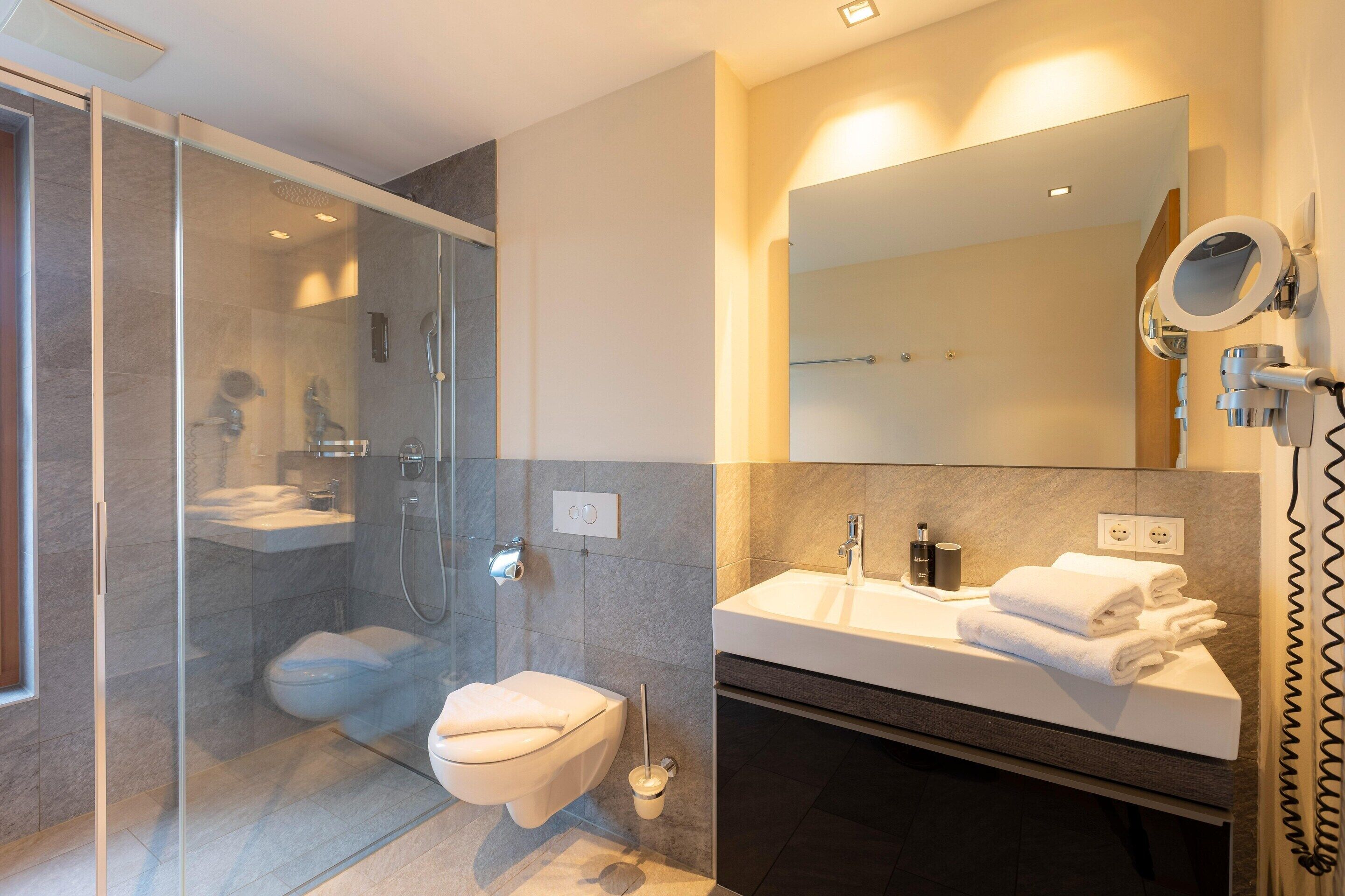 A modern bathroom with a glass-enclosed shower, a toilet, and a vanity with a mirror and towel rack.