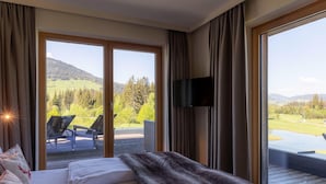 Une chambre d’hôtel avec un grand lit, une télévision et un balcon offrant une vue sur un terrain de golf et les montagnes.