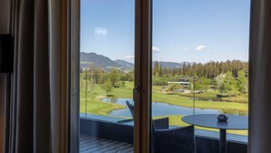 Un balcon offrant une vue sur un terrain de golf, un étang et des montagnes au loin.