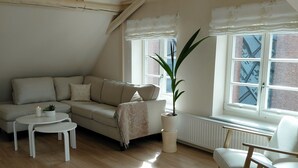 Ein gemütliches Loft mit hohen Decken, freiliegenden Balken, einem großen Fenster mit Stadtblick, einer Couch, einem Couchtisch und einem Blumentopf.
