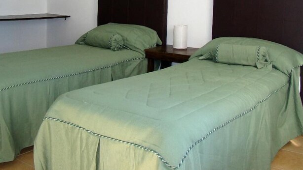 A room with two single beds, each with a dark headboard and green bedding. There is a small table with a white candle between the beds. - Colon Village (Colon)