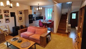 A spacious living room with a sofa, coffee table, and a dining area with chairs and a table. There is a staircase leading to another level. - Pretty house with garden in the heart of a Corrèze village (Chamberet)