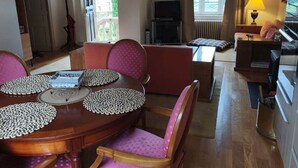 A dining area with a wooden table and pink chairs, a television, and a window with curtains. - Pretty house with garden in the heart of a Corrèze village (Chamberet)