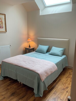 Ein Schlafzimmer mit Dachfenster, einem Bett mit hellblauer Bettwäsche, einer Nachttischlampe und einem Heizkörper.