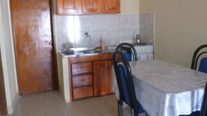 A kitchen with wooden cabinets, a tiled backsplash, a stove, and a dining table with chairs. - Guatambú Apart Hotel (Puerto Iguazú)