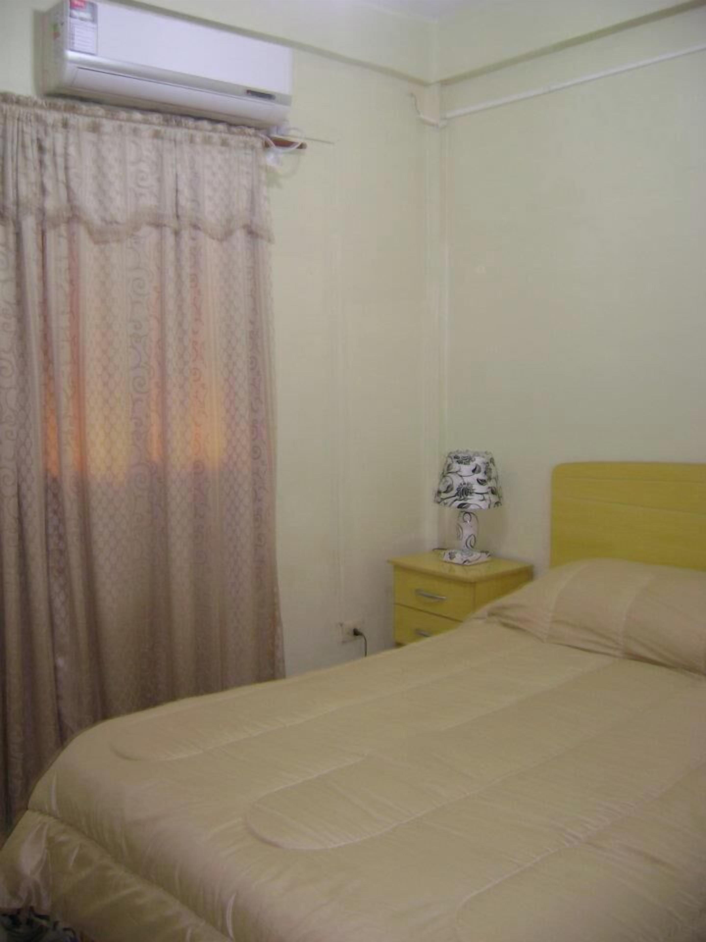 Un letto singolo con testiera, un comodino con una lampada e una tenda.